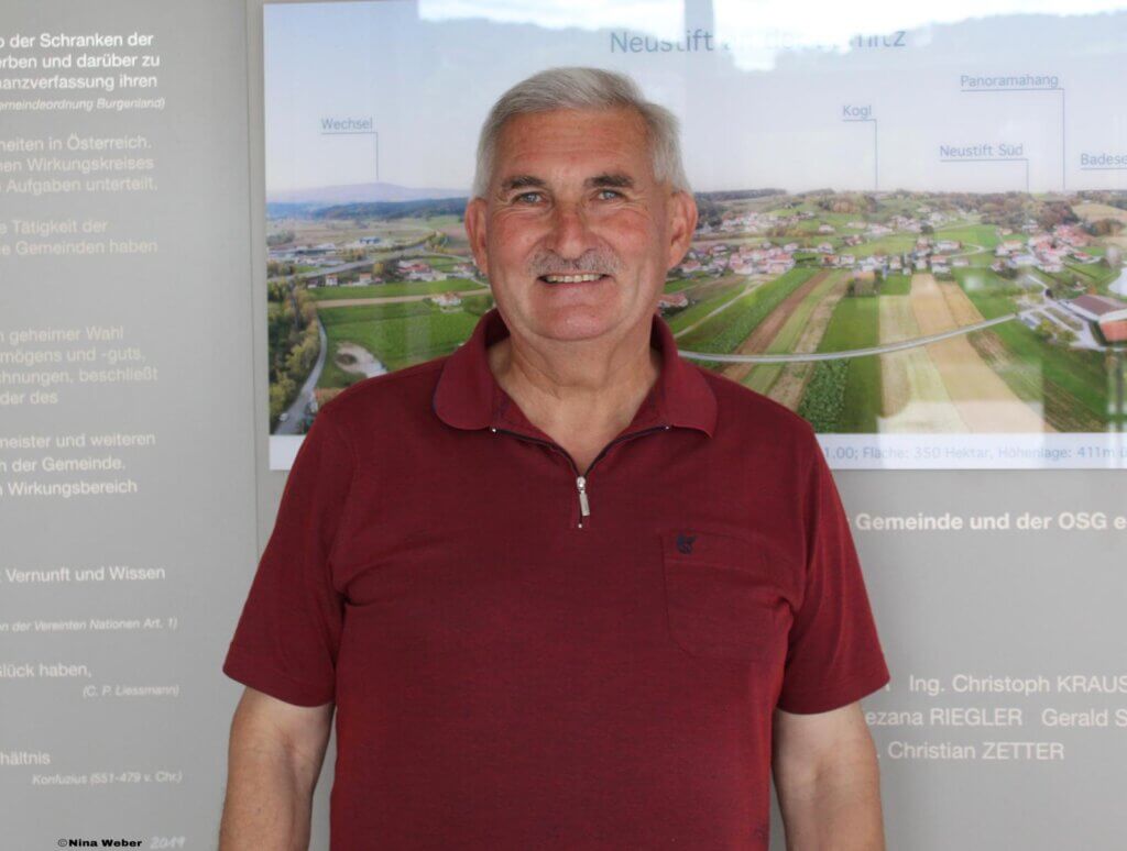 Auf diesem Bild sieht man Bürgermeister Johann Kremnitzer mit einem roten Shirt. Er steht vor einer Informationstafel.