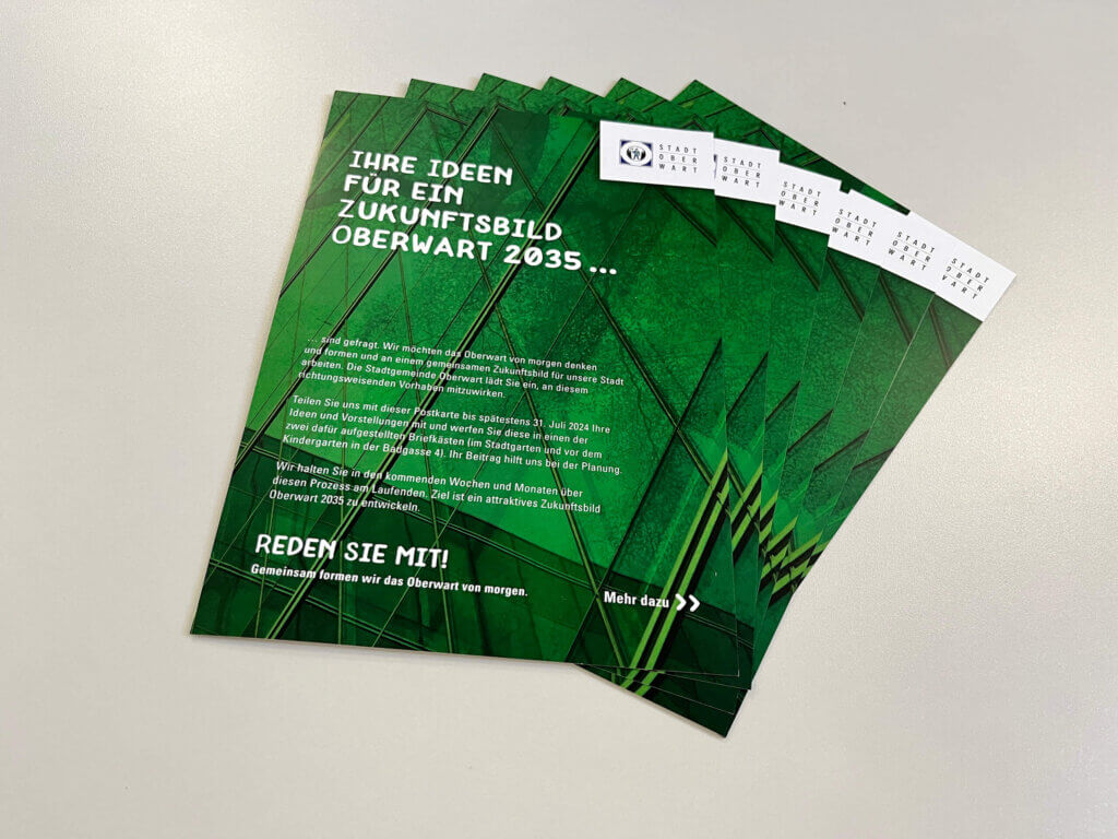 Auf diesem Bild seiht man Flyer mit dem Thema "Ihre Ideen für ein Zukunfstbild Oberwart 2035...". Die Flyer sind Grün mit weißer Schrift .