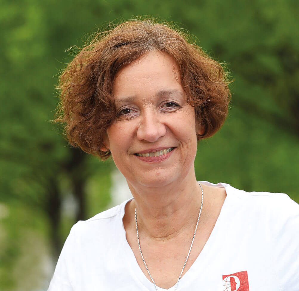 Auf diesem Bild sieht man Barbara Kopf. Sie lächelt und trägt ein weißes Shirt. Sie hat kurze braune Haare.