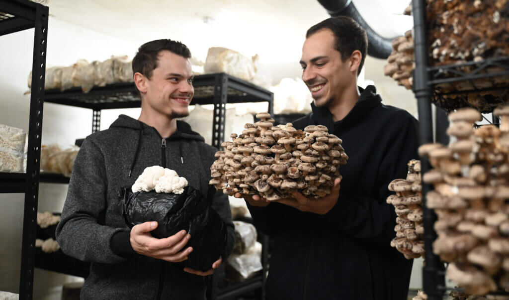 Auf diesem Bild sieht man Philipp Maitz und Daniel Kirnbauer wie sie Pilze in der Hand halten und dabei lächeln.