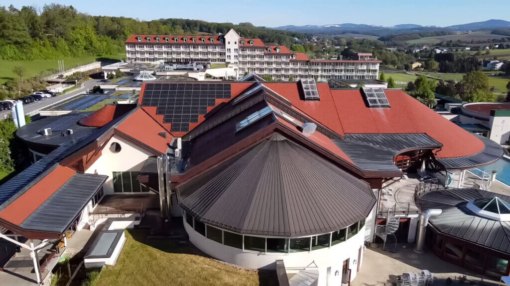 Ein weiteres Luftbild des Avita Resorts, das die roten Dächer und die weitläufige Anlage mit mehreren Gebäuden zeigt. Im Hintergrund sind grüne Hügel und Wälder sichtbar.