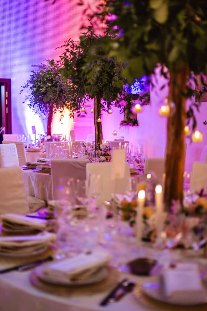 Elegant gedeckter Hochzeitstisch mit Kerzenlicht und floraler Dekoration unter Lichterketten in einem festlichen Saal.